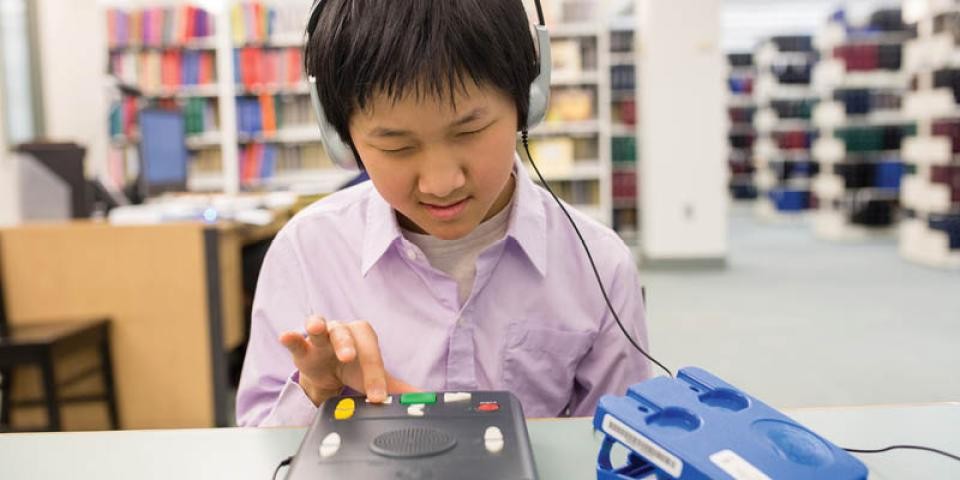 A boy sits in a library using a talking book device. 