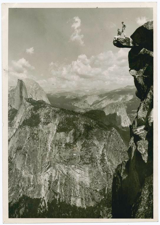 two men stand on a high ledge with Sierra mountains in distance