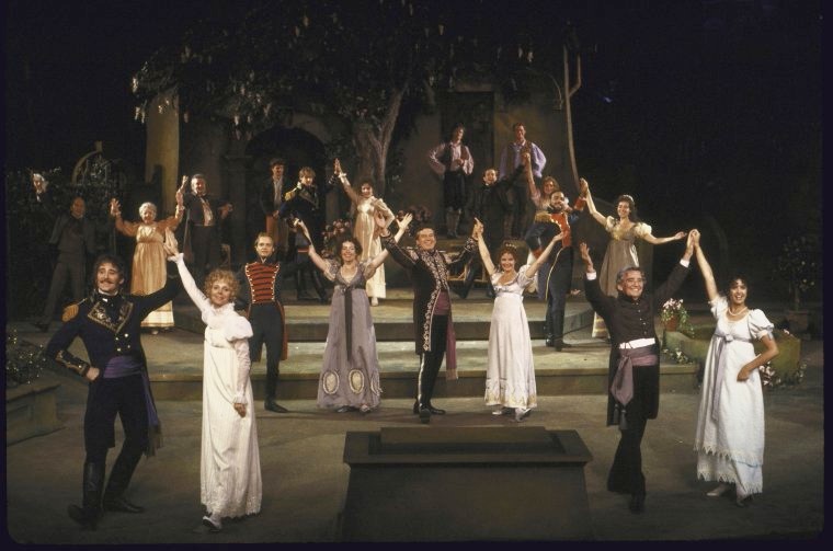 large cast on stage with arms raised
