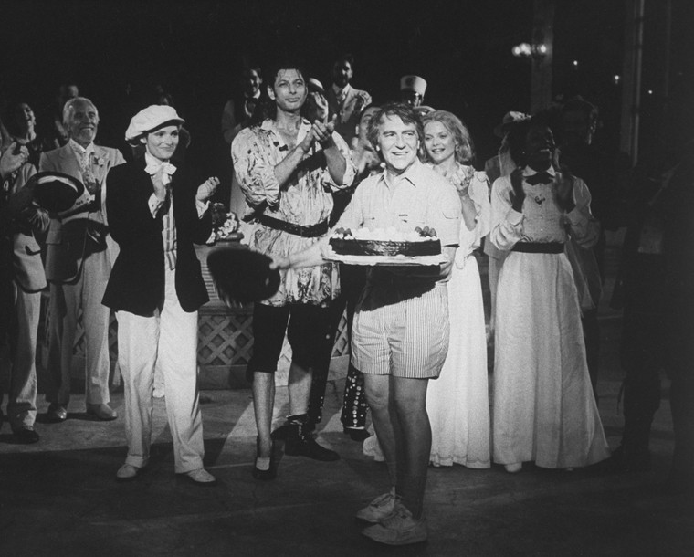 man on stage smiling as cast members cheer
