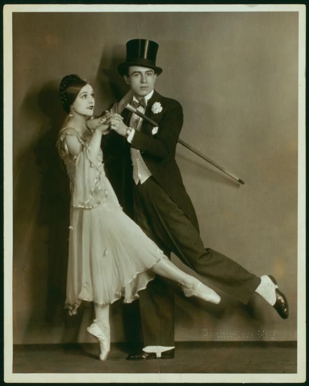 A man and woman dancing. He is wearing a top hat and holding a cane.