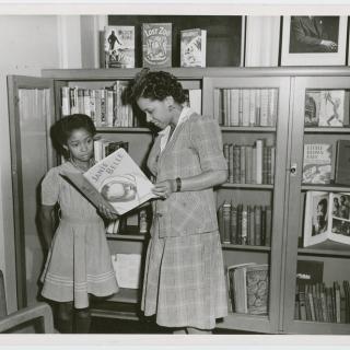 Librarian Augusta Baker showing a copy of Ellen Tarry's "Janie Belle" to a young girl at the library
