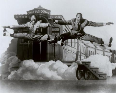 Two dancers doing high jumps in front of an image of a steam engine. 